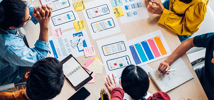 A team works on a project at a table with drawings and sticky notes