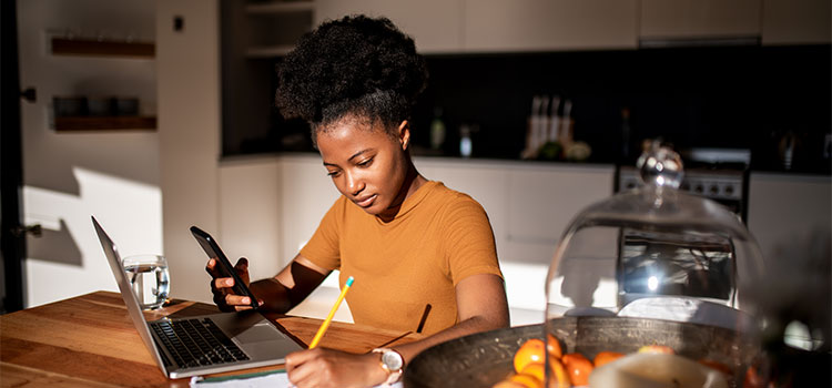 A woman taking notes and working on her laptopma