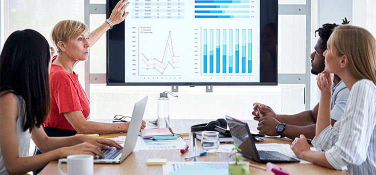 a woman explains business charts to others sitting at a table in an office