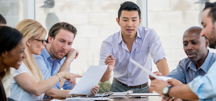 a man leans over a table as he explains information that coworkers are reading