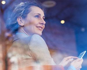 mature woman looking out window while on smart phone