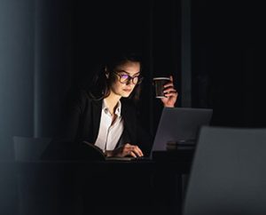 woman holds coffee cup in dark room while on laptop