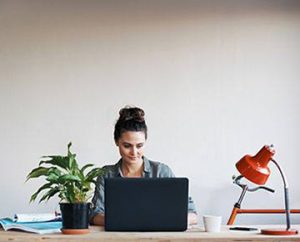 woman with plant on desk reviews info on laptop