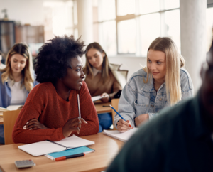 two diverse college students seated and talking in a classroom