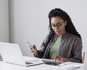 woman accountant with bachelors checks data accuracy on mobile and calculator